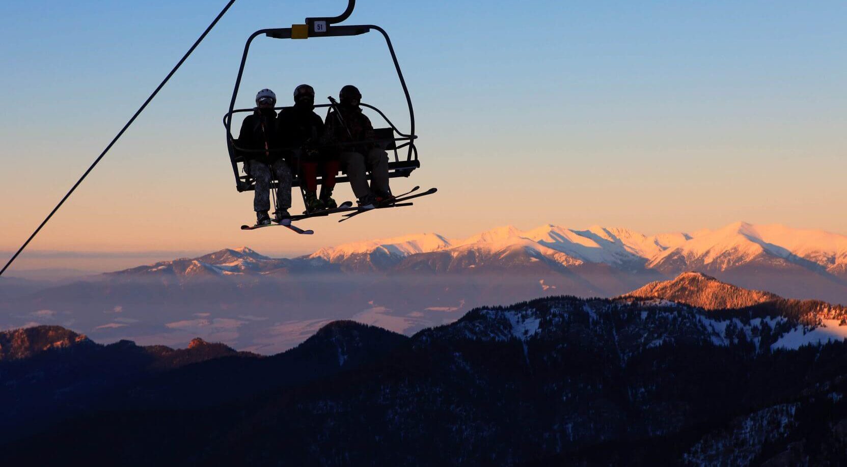 Troje ludzi w strojach narciarskich na wyciągu, w tle piękny widok