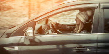 Kobieta w zimowej czapce za kierownicą auta. W tle zimowa sceneria