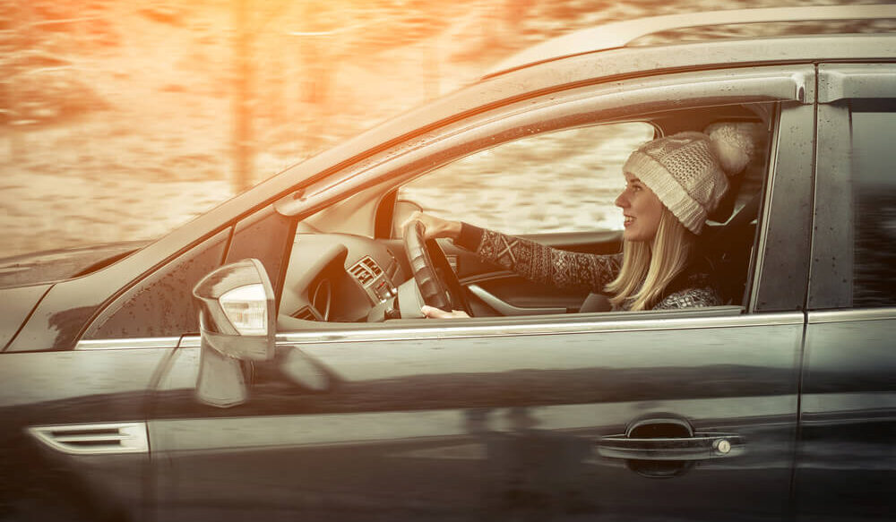 Kobieta w zimowej czapce za kierownicą auta. W tle zimowa sceneria