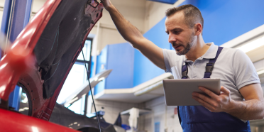 Mechanik samochodowy pochyla się nad otwartą maską samochodu