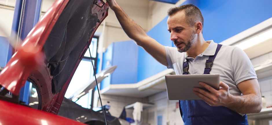 Mechanik samochodowy pochyla się nad otwartą maską samochodu