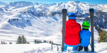 Rodzic z dzieckiem siedzący na stoku i patrzący na ośnieżone Alpy