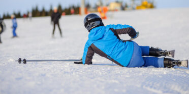 Człowiek w kasku i kombinezonie narciarskim leżący na ośnieżonym stoku