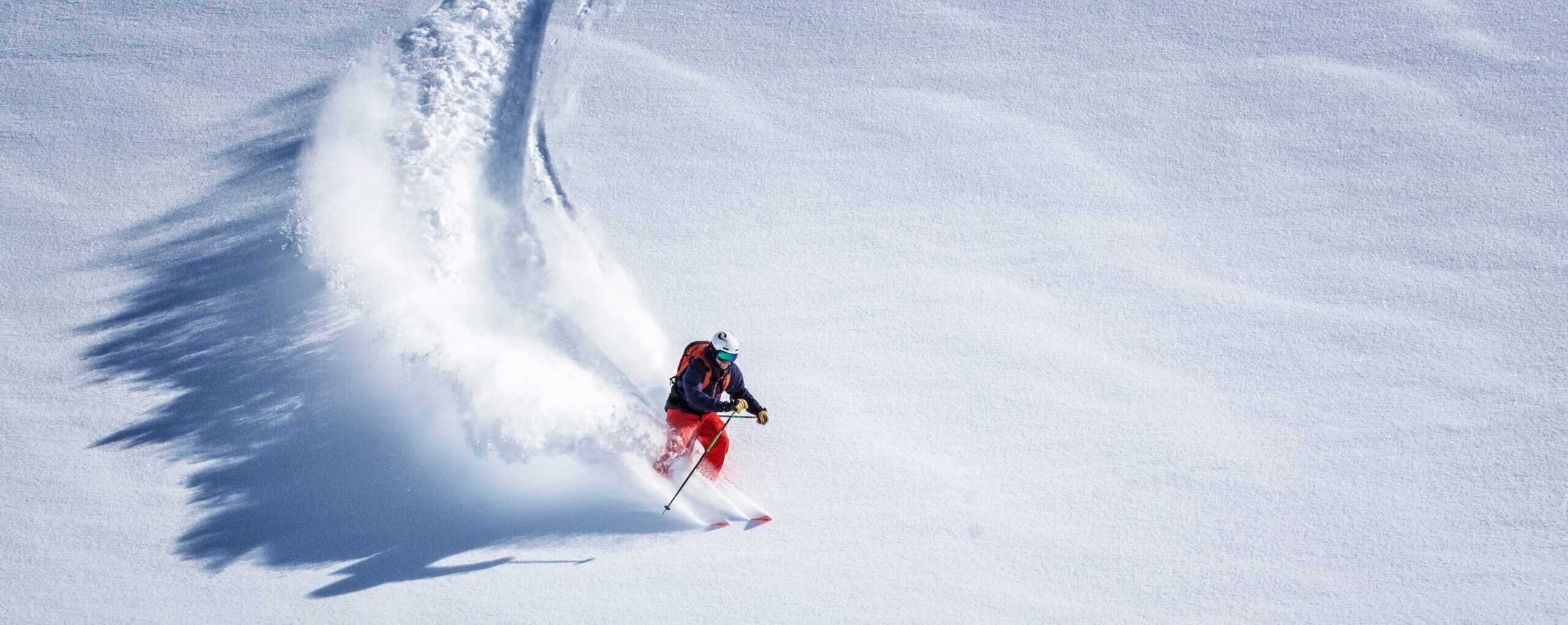 Narciarz zjeżdżający ze stoku, za nim wzburzony śnieg