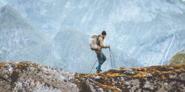 Turysta z plecakiem i kijami trekkingowymi idzie po szlaku w górach