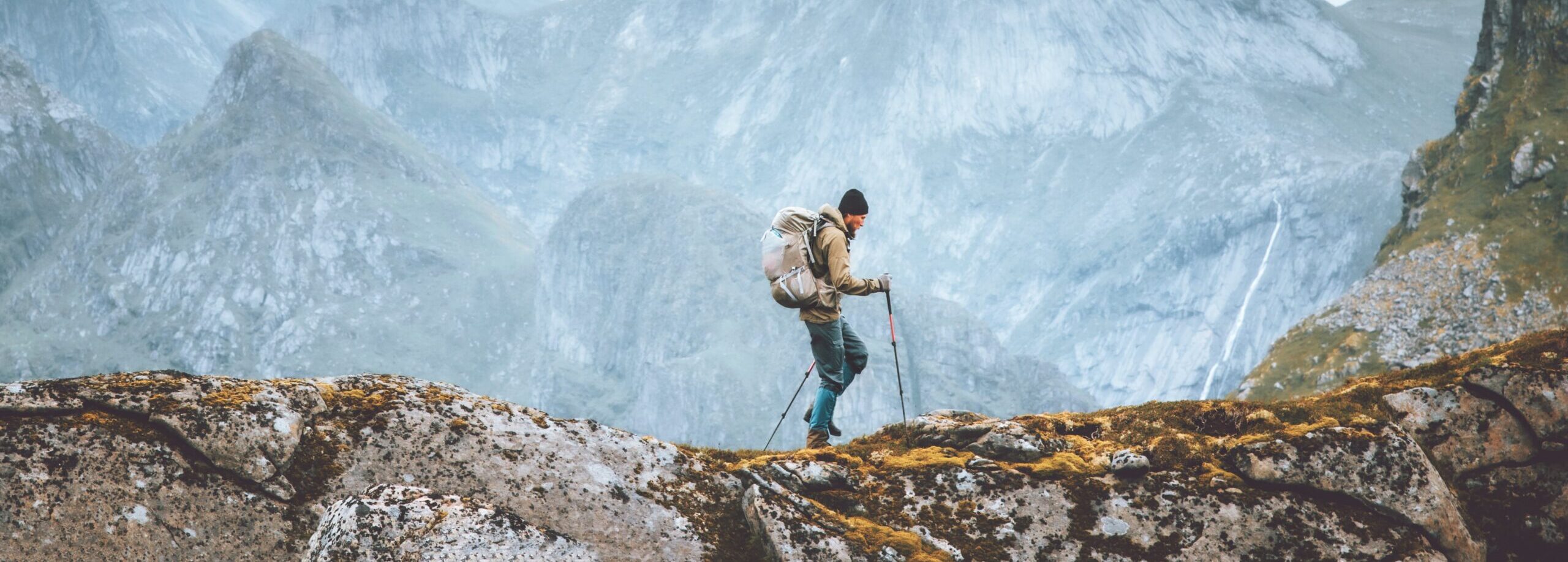 Turysta z plecakiem i kijami trekkingowymi idzie po szlaku w górach