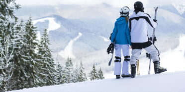 Para w strojach narciarskich na ośnieżonym stoku, podziwia widoki.