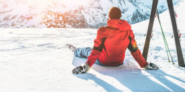 Mężczyzna w stroju narciarskim siedzący na stoku, patrzący na ośnieżone góry
